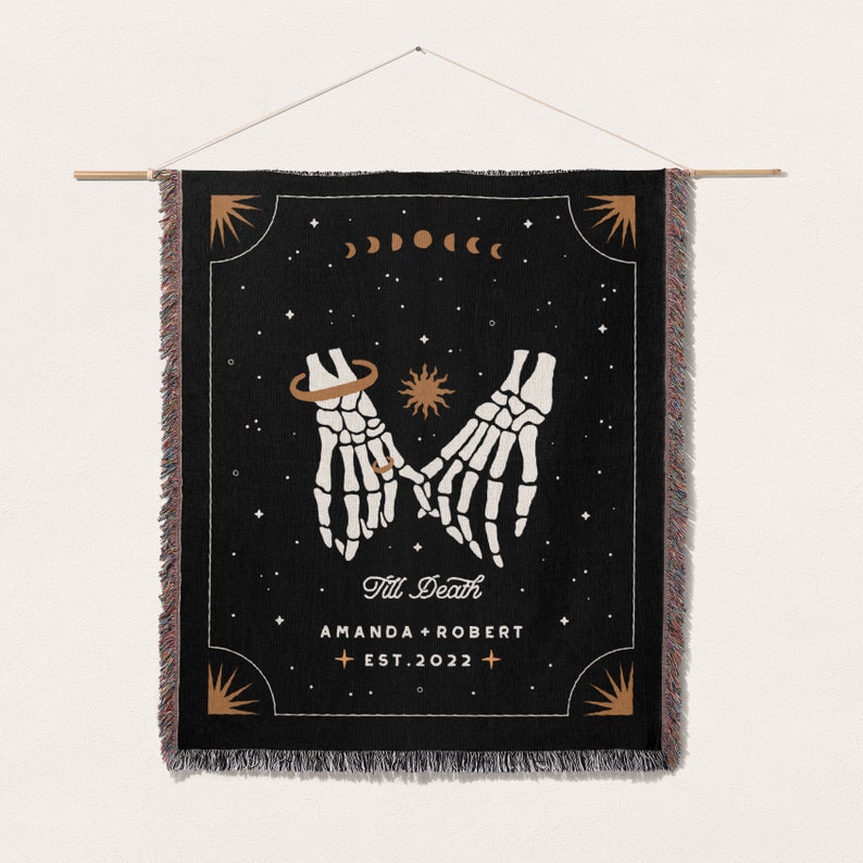 May include: Black woven tapestry featuring a design of two skeleton hands holding each other, with a ring on one finger. The text 'Till Death' is written below the hands, followed by 'Amanda + Robert Est. 2022'.