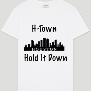 May include: White t-shirt with a black graphic design featuring the text "H-Town" above a skyline silhouette of Houston, Texas, and the text "Hold It Down" below.