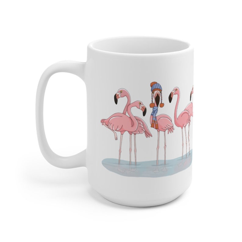 May include: White ceramic mug featuring a design of pink flamingos. The flamingos are standing in a line in water, and one flamingo is wearing a blue hat and scarf.