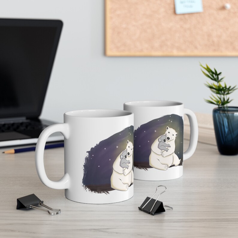 Pu&ograve; includere: Due tazze in ceramica bianca con un design di un orso polare che abbraccia un koala su uno sfondo di notte stellata blu scuro.