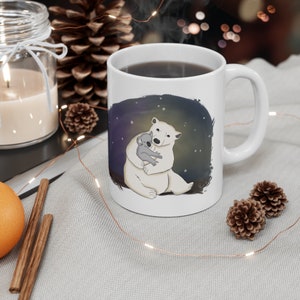 Pu&ograve; includere: Tazza in ceramica bianca con un'immagine di un orso polare che tiene un koala. Lo sfondo &egrave; blu scuro con stelle bianche.