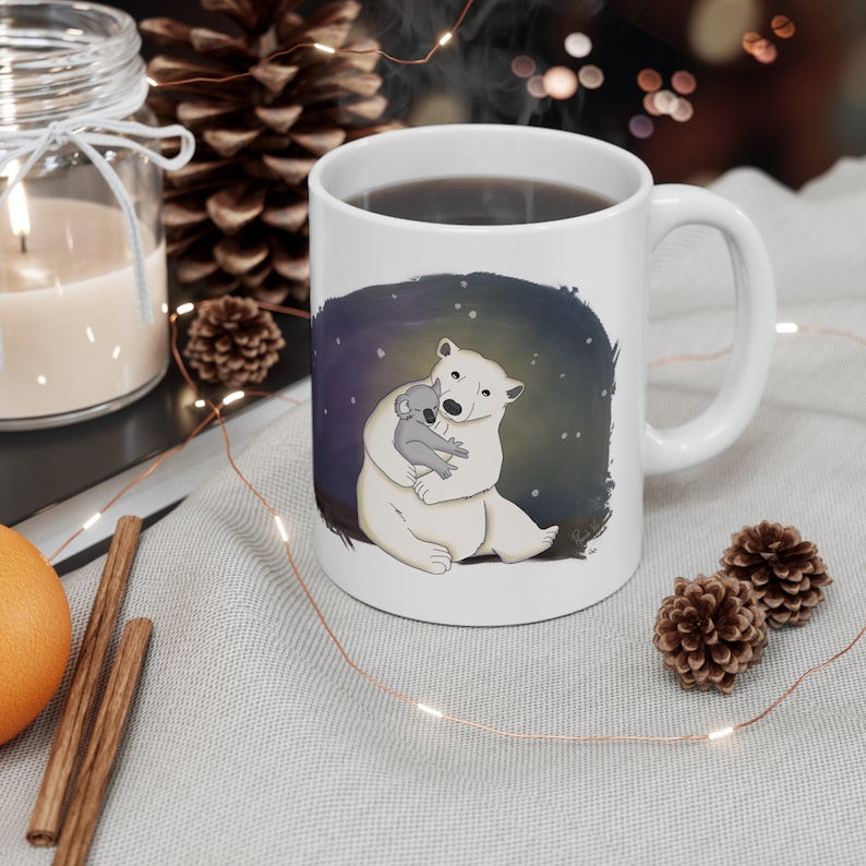 Pu&ograve; includere: Tazza in ceramica bianca con un'immagine di un orso polare che tiene un koala. Lo sfondo &egrave; blu scuro con stelle bianche.