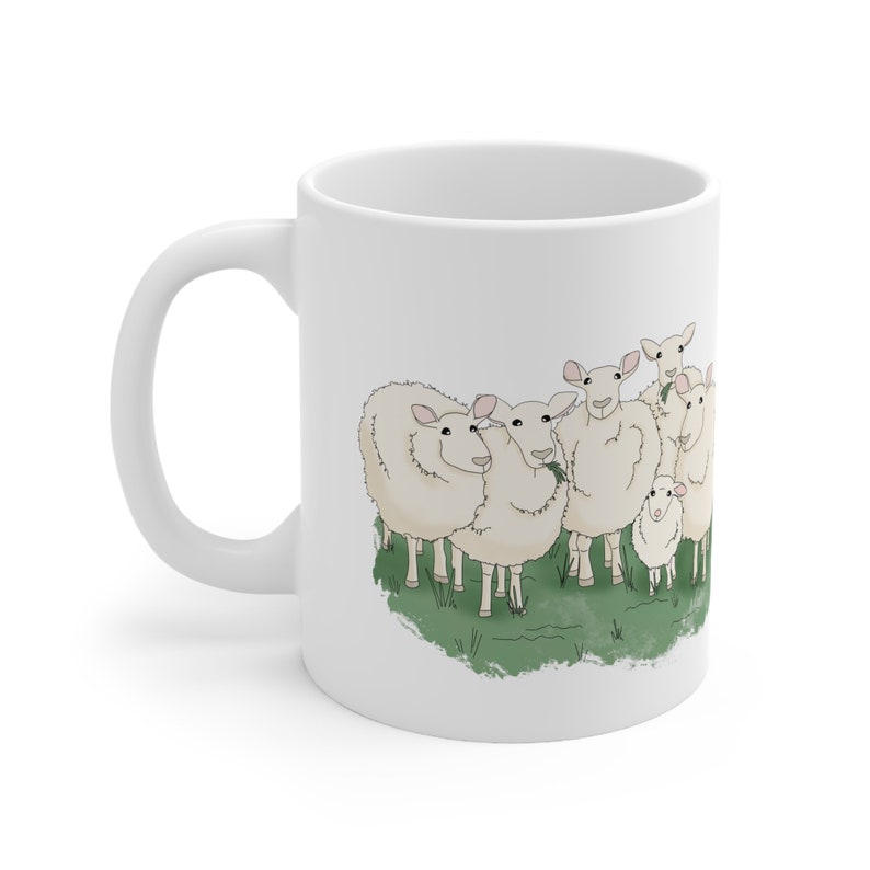 Op de afbeelding: Witte keramische koffiemok met een cartoonillustratie van een groep schapen die in een veld met groen gras staan.