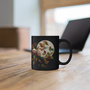 Pu&ograve; includere: Tazza in ceramica nera con un gufo bianco che vola attraverso una luna piena con foglie autunnali. Il gufo ha piume marroni e bianche.