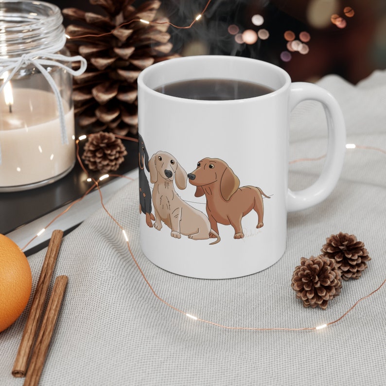 May include: White ceramic coffee mug with a black, brown, and cream dachshund illustration. The mug has a black handle and is filled with coffee.