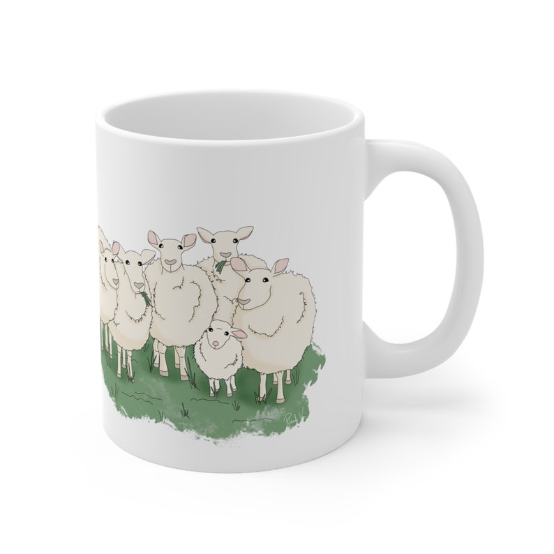 Op de afbeelding: Witte keramische mok met een cartoonillustratie van een groep schapen die in een veld met groen gras staan. De schapen zijn allemaal wit met zwarte ogen en roze neuzen.