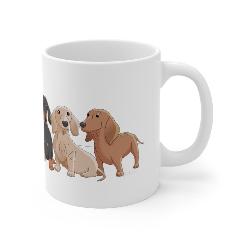 May include: White ceramic coffee mug with a design of four dachshund dogs in different colors. The dogs are facing the left side of the mug.