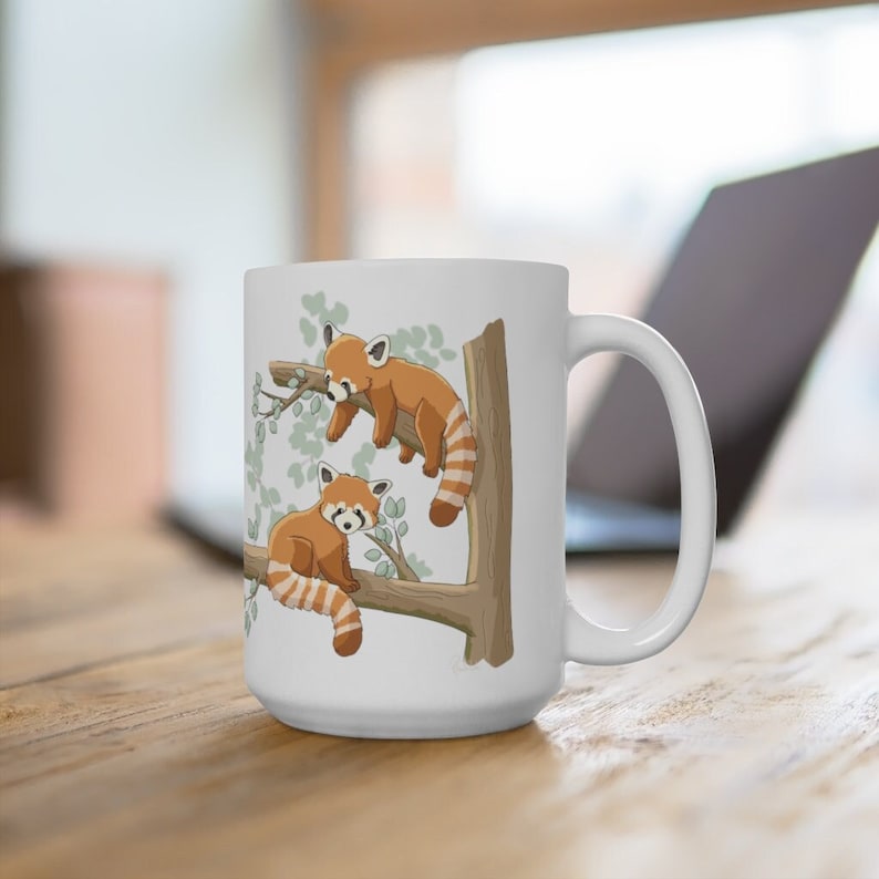 May include: White ceramic mug with a red panda design. Two red pandas are perched on a tree branch with green leaves. The mug has a white handle.