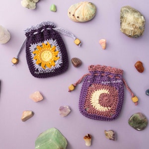 May include: Two crocheted pouches with a purple and lavender color scheme. One pouch features a yellow sunflower design and the other features a white crescent moon design. Both pouches are surrounded by various crystals and stones on a purple background. The text "Alyssa Creates" is visible on both pouches.