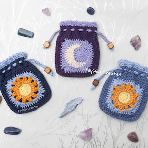 May include: Three crocheted drawstring pouches with different designs. The pouches are blue, purple, and light blue. The designs are a sun, a moon, and a flower. The pouches are on a white background with small stones.