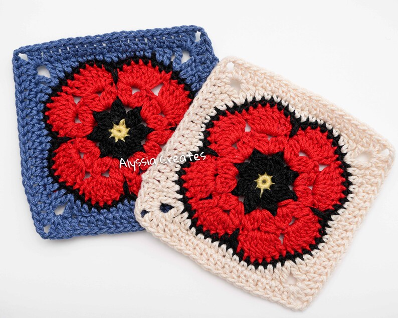 May include: Two crocheted squares with a floral design. One square is blue with a red, black, and yellow flower. The other square is off-white with a similar red, black, and yellow flower. The squares are handmade and feature a textured stitch.