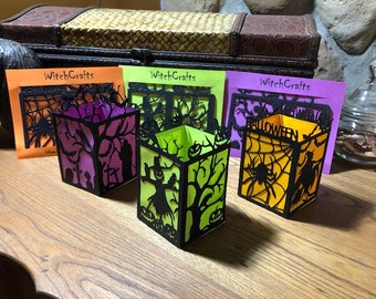 May include: A collection of Halloween-themed paper lanterns with intricate black cut-out designs. Each lantern features a different color scheme and design, including spiders, trees, and the word "Halloween". The background cards say "WitchCrafts".
