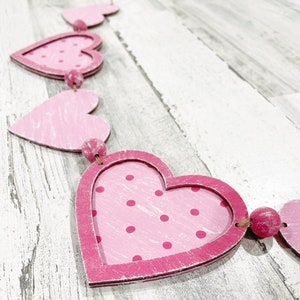 K&ouml;nnte beinhalten: Eine rosa und wei&szlig;e Herzgirlande mit rosa Punkten. Die Girlande ist aus Holz und hat einen rustikalen Look.