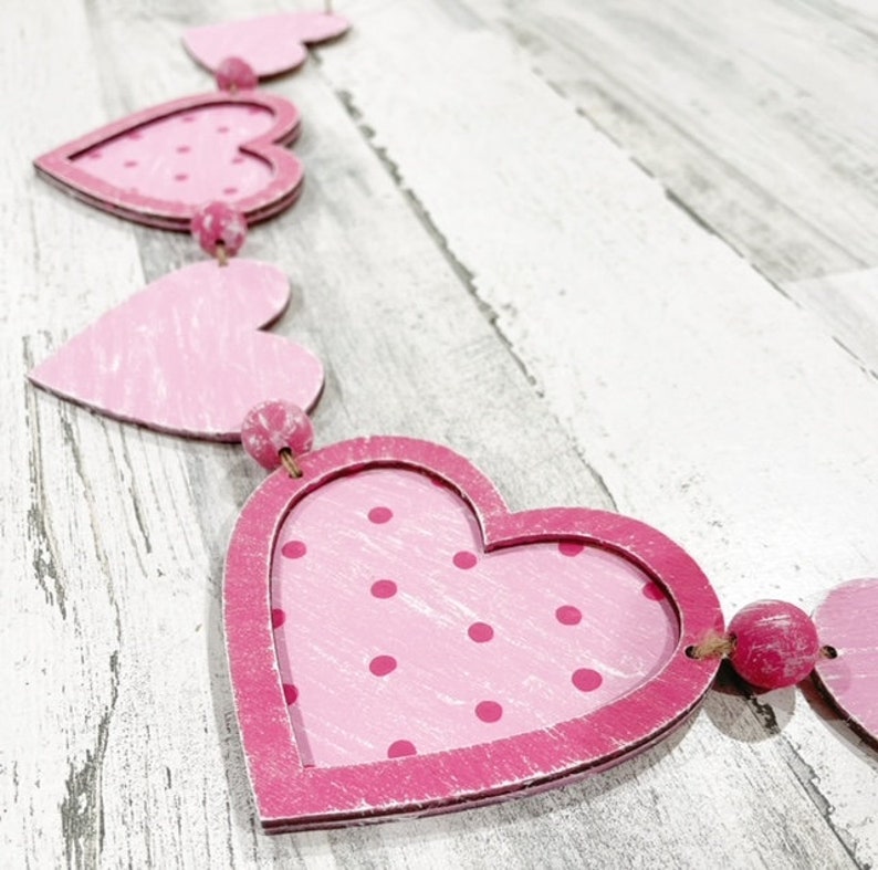 K&ouml;nnte beinhalten: Eine rosa und wei&szlig;e Herzgirlande mit rosa Punkten. Die Girlande ist aus Holz und hat einen rustikalen Look.