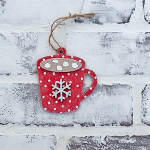 May include: Red and white wooden ornament shaped like a mug with white polka dots and a snowflake design. The mug has a brown rim and white marshmallows on top.