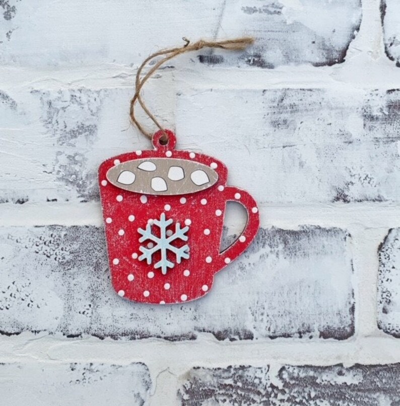 May include: Red and white wooden ornament shaped like a mug with white polka dots and a snowflake design. The mug has a brown rim and white marshmallows on top.