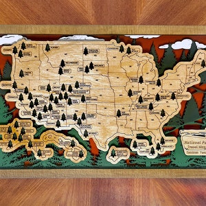 May include: A layered wooden wall map of the United States featuring cutouts for each state and small tree icons marking national parks. The map includes text labels for parks and states, with a sign in the corner reading National Park Travel Map.