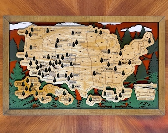May include: A layered wooden wall map of the United States featuring cutouts for each state and small tree icons marking national parks. The map includes text labels for parks and states, with a sign in the corner reading National Park Travel Map.