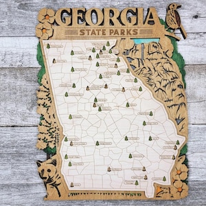 May include: A wooden map of Georgia State Parks with the names of each park printed on the map. The map is surrounded by a decorative border with flowers and a bird.