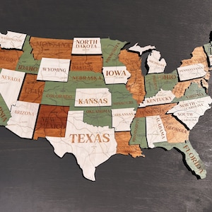 May include: A wooden map of the United States with each state outlined and labeled. The states are painted in shades of brown, green, and white.