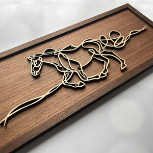May include: Wooden wall art featuring a running horse silhouette. The horse is crafted from light-colored wood and mounted on a dark brown wooden rectangular frame. The artwork is a minimalist design, suitable for home decor.