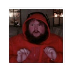 May include: A sticker featuring a person wearing a red hoodie and a headset. The person has a beard and is looking forward with a surprised expression. The background is blurred.