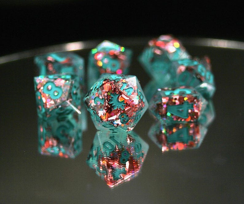K&ouml;nnte beinhalten: Satz tealfarbener und rosafarbener Glitzerw&uuml;rfel mit Zahlen auf jeder Seite. Die W&uuml;rfel sind aus Harz und haben eine glitzernde Oberfl&auml;che.