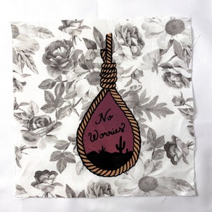 May include: A white fabric with a floral pattern featuring a hand-painted noose with a purple drop and the text "No Worries?" in black cursive.