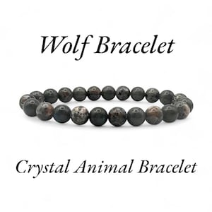 May include: A beaded bracelet with dark gray and brown stones. The bracelet is labeled "Wolf Bracelet" and "Crystal Animal Bracelet" in black text. The beads are round and appear to be made of a natural stone.
