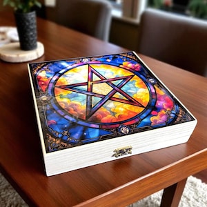 May include: A white wooden box with a colorful stained-glass design on the lid. The design features a five-pointed star within a circle, set against a backdrop of clouds in shades of blue, yellow, and orange.
