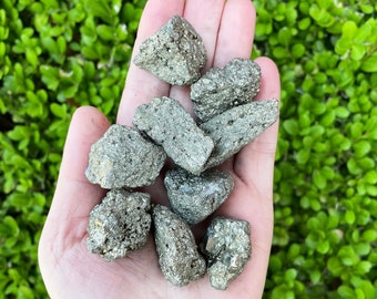 May include: A hand holding a collection of small, rough, gray and silver pyrite stones.