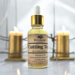 May include: A gold bottle with a dropper top and a label that reads "WINSLOW NATURALSO Cutting Tie (for severing soul bonds) Intention Oil Handcrafted with cleansed herbs, crystals, and oils To be used for ritual work & topical skin use NET WT. 1oz (30ml)"