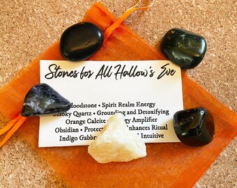 May include: A set of five stones in a small orange drawstring bag. The stones are black, grey, and white. A card with the text "Stones for All Hallow's Eve" is visible in the bag. The card lists the names of the stones and their properties.