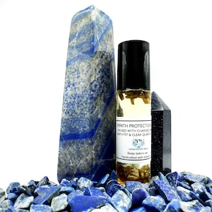 May include: A glass roller bottle with a black cap filled with a clear liquid and small pieces of dried herbs. The bottle is labeled "Empath Protection" and "Winslow Naturals". The bottle is surrounded by blue and white stones.
