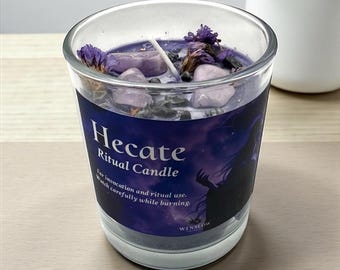 May include: A glass candle labeled "Hecate Ritual Candle" with a purple wax interior. The candle is decorated with purple flowers and stones. The label features a silhouette of a figure and the text "For invocation and ritual use. Watch carefully while burning."