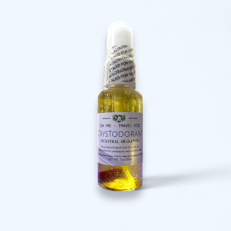 May include: A clear glass travel-size bottle of Crystodorant, with a white cap and a label that reads "Ancestral Awakening." The bottle contains a yellow liquid with visible particles. The net weight is 1 oz.
