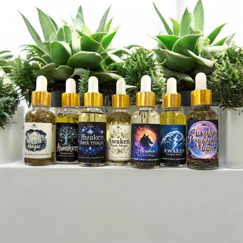 Puede incluir: Una colecci&oacute;n de frascos cuentagotas de vidrio llenos de aceites herbales. Cada frasco tiene una tapa dorada y una etiqueta con textos como "Awaken Nature Magic" y "Awaken Dark Magic". Los frascos est&aacute;n frente a plantas verdes.
