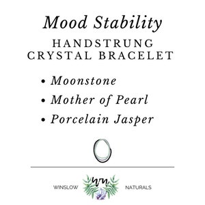 May include: A hand-strung crystal bracelet with moonstone, mother of pearl, and porcelain jasper beads. The bracelet is green, white, and black. The text "Mood Stability" is at the top of the image. The text "HANDSTRUNG CRYSTAL BRACELET" is below the title. The text "Moonstone", "Mother of Pearl", and "Porcelain Jasper" are listed below the title. The text "WINSLOW NATURALS" is at the bottom of the image.