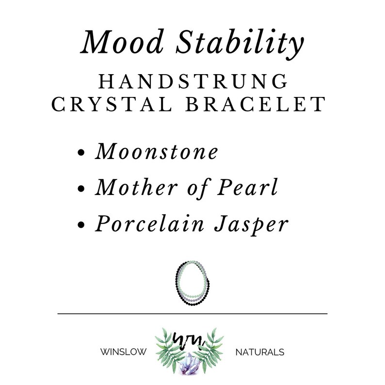 May include: A hand-strung crystal bracelet with moonstone, mother of pearl, and porcelain jasper beads. The bracelet is green, white, and black. The text "Mood Stability" is at the top of the image. The text "HANDSTRUNG CRYSTAL BRACELET" is below the title. The text "Moonstone", "Mother of Pearl", and "Porcelain Jasper" are listed below the title. The text "WINSLOW NATURALS" is at the bottom of the image.
