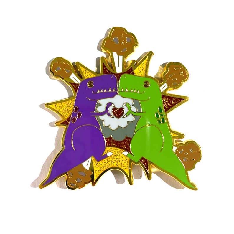 Peut inclure: &Eacute;pingle en &eacute;mail dor&eacute;e repr&eacute;sentant deux dinosaures de dessin anim&eacute;, un violet et un vert, se faisant face. Ils sont positionn&eacute;s devant un nuage blanc avec un c&oelig;ur. L'&eacute;pingle a un fond dor&eacute; scintillant et des accents marron.