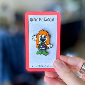 Puede incluir: Un colorido pin de esmalte con un personaje de dibujos animados con pelo naranja, auriculares y una camiseta negra con un dise&ntilde;o pixelado. El pin est&aacute; en una tarjeta roja con el texto "Queen Pin Designs". El personaje lleva zapatos verdes y el texto "NO WAY!!" est&aacute; en la camiseta.
