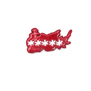 May include: A red enamel pin in the shape of a stylized map with five white flower-shaped cutouts. The pin has a glossy finish and is set against a white background.