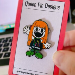 Puede incluir: Un pin de esmalte colorido con un personaje de dibujos animados con pelo naranja, auriculares y un atuendo negro con el texto "NO WAY!!". El pin est&aacute; en una tarjeta con bordes rojos con "Queen Pin Designs" y la direcci&oacute;n del sitio web.
