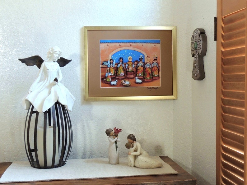 May include: A framed print of a Nativity scene with a gold frame hangs on a wall. A white angel statue with black wings sits atop a black and white metal lantern. Two small figurines and a decorative cross are also visible.