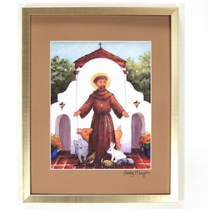 May include: A framed print of a painting depicting Saint Francis of Assisi standing in front of a white building with a cross on top. He is surrounded by animals, including a deer, a rabbit, a cat, a bird, and a turtle. The painting is signed "Cindy Mayer" in the bottom right corner.