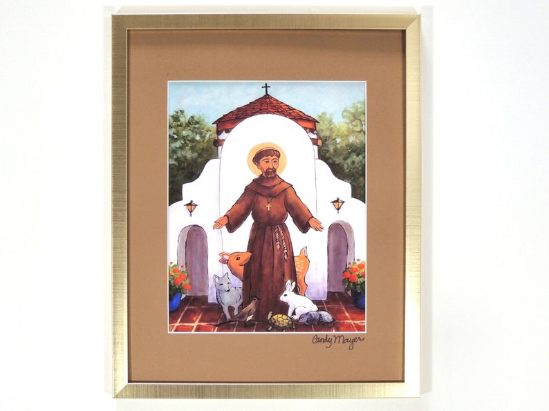 May include: A framed print of a painting depicting Saint Francis of Assisi standing in front of a white building with a cross on top. He is surrounded by animals, including a deer, a rabbit, a cat, a bird, and a turtle. The painting is signed "Cindy Mayer" in the bottom right corner.