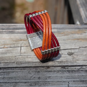 May include: A braided leather bracelet with a silver clasp. The bracelet is made of five strands of leather, two red and three orange.