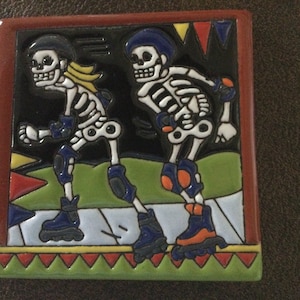 May include: Two colorful ceramic tile skeletons wearing roller skates and knee pads. The skeletons are on a green and white background with red, yellow, and blue triangles.