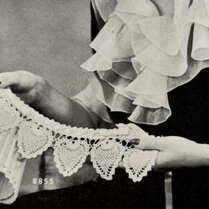 Puede incluir: Primer plano de un borde de encaje de ganchillo blanco con un borde festoneado y un diseño en forma de corazón. El borde está sostenido por una mano y el número 8855 es visible en la esquina inferior izquierda.