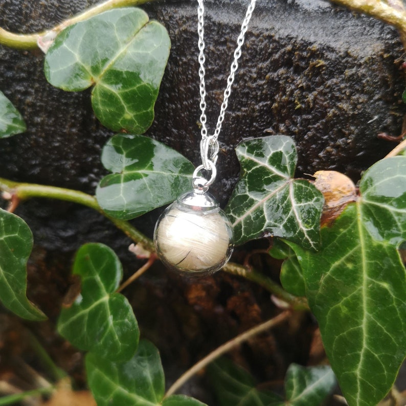 May include: A silver chain necklace with a clear glass orb pendant containing a swirl of light brown hair.